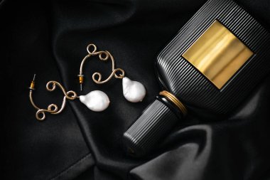 Siyah ipeksi kumaş üzerinde lüks parfüm şişesi olan zarif inci küpeler. Yukarıdan görüntüle