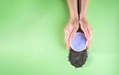 Kadının elleri mor nemlendirici krem ve bakuchiol karışımı tutuyor. Babchi tohumları (Psoralea corylifolia). Bakuchiol kozmetik konsepti. Düz konum, kopyalama alanı, dikey.