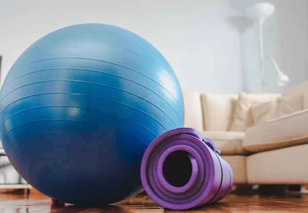 Blue fitness ball and rolled fitness mat in the living room. Unfocus couch on background. Home workout concept.