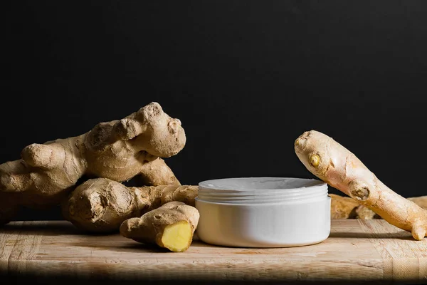 Cosmetics body cream container with ginger oil extract on wooden table. ginger roots and slices. Ginger oil extract cosmetics concept. — Stock Photo, Image
