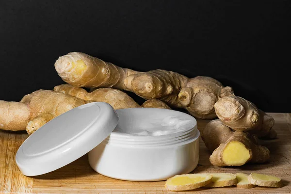 Cosmetics body cream container with ginger oil extract on wooden table. ginger roots and slices. Ginger oil extract cosmetics concept. — Stock Photo, Image