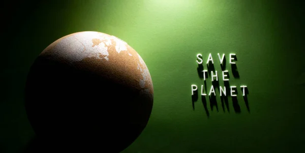 Cork globe with text "Save the planet" on the right under soft light in dark key. Save the planet Earth concept. Environmental conservation concept. Flat lay, green background. — Stock Photo, Image