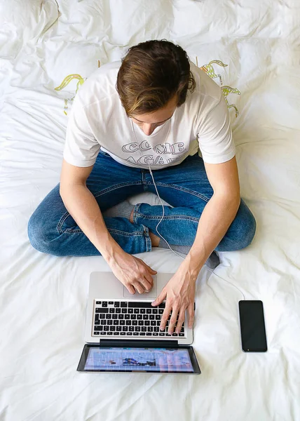 Laptop Bilgisayar Akıllı Telefonla Çalışan Genç Adam Yatakta Oturuyor — Stok fotoğraf