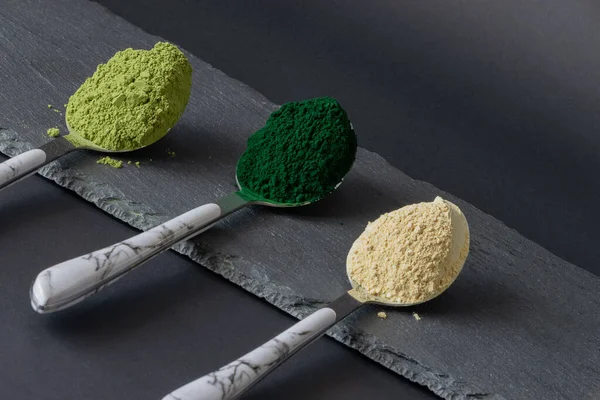汤匙上有螺旋藻，马沙和玛卡粉在黑色石板上。 角度图像。 超级食品粉末概念. — 图库照片