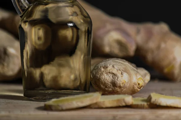 Ginger oil bottle with ginger roots and slices on wooden cutting board. Healthy eating concept. Close up, black background. — Stock Photo, Image