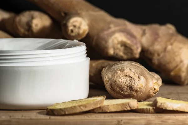 Contenedor de crema corporal cosmética con extracto de aceite de jengibre en mesa de madera. raíces de jengibre y rebanadas. Aceite de jengibre extracto concepto de cosméticos . — Foto de Stock