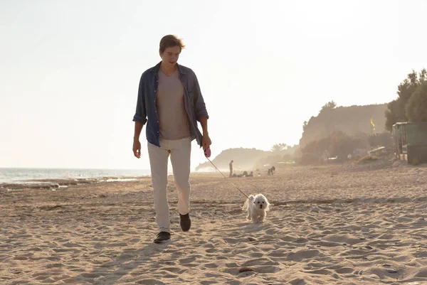 年轻人带着狗在海滩上散步 — 图库照片