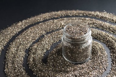 Siyah arka planda chia tohumları olan küçük bir kavanoz. Uzayı kopyala Chia süper yiyecek malzemesi konsepti.