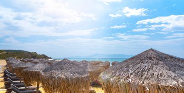 Konforlu şezlongları ve saman şemsiyeleriyle Idyllic plajının panoramik manzarası. Konfor yaz tatili konsepti
