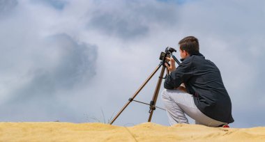 Adam kum tepelerinde fotoğraf ve video çekmek için cep telefonunu tripoda kuruyor. Arka planda bulutlu bir gökyüzü. Seyahat fotoğrafçısı konsepti.