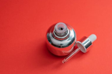 Kırmızı arka planda cam pipetli lüks kozmetik şişesi ve mesaj için yer var. - Bakuchiol konsepti. Retinol alternatifi.