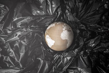 Siyah plastik torbalar arasında Dünya 'yı temsil eden mantar küre batıyor. Okyanus plastik kirliliği sorunu kavramı.