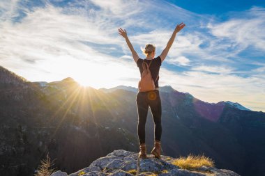 Sırt çantalı genç bir kadın kayalık uçurumun kenarında durup dağlarda gün batımını seyrediyor. Motivasyon ve ilham, özgürlük kavramı. Boşluğu kopyala.