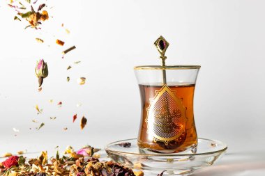 Geleneksel Türk siyah çayı (Osmanlı Mehmet V 'in tugra imzasıyla) ve altın kaşık ametist. Düşen çay otları ve solda kurumuş çiçekler. Beyaz arkaplan.
