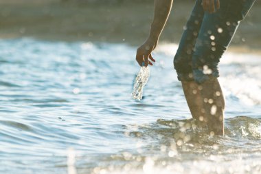 Gönüllü adam denizden plastik şişe çöpü topluyor. Aşağıdan manzara, dalgalar, gün batımı, su sıçraması. Okyanus konseptini temizlemek. 