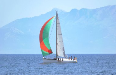 Gündüz açık denizde renkli yelkenli bir yat ve arka planda bir ada. Yachting macera konsepti