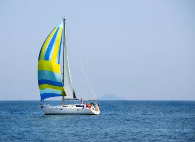 Gündüz sakin denizde renkli yelkenli bir yat ve açık mavi bir gökyüzü. Yachting macera konsepti