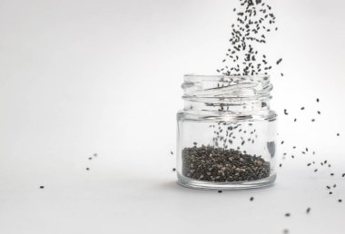 Beyaz arka planda cam kavanoza kuru chia tohumları dökülüyor. İzole edilmiş, kopyalama alanı. Chia süper yemek paleo diyet konsepti.
