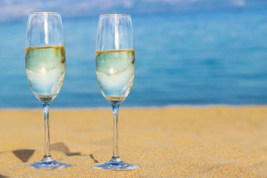 Mavi denize karşı kumlu sahilde iki bardak şampanya. Yaz konseptini kutla