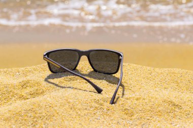Kumsalda modern güneş gözlüğü. Arka planda odaklanmamış deniz. Yakın manzara, yaz tatili konsepti.