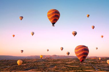 Güneş doğarken vadilerin ve tarlaların üzerinde uçan renkli sıcak hava balonları. Türkiye, Kapadokya.