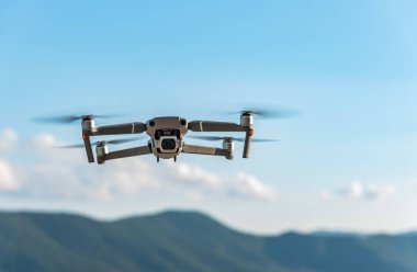 Arka planda dağlar olan İHA gökyüzünde uçuyor