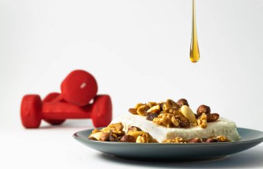 Kuru fındıklı soya süzme peynir ve siyah tabağa düşen bal damlası. Arka planda odaklanmamış kırmızı dambıllar. Protein beslenme vejetaryen spor yemekleri. 