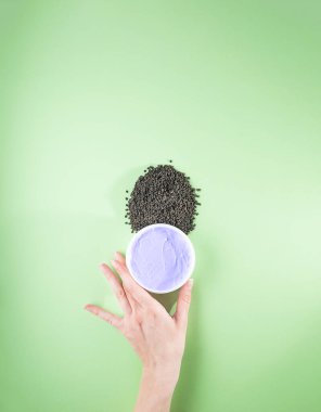Kadının elinde mor nemlendirici krem ve bakuchiol var. Babchi tohumları (Psoralea corylifolia). Bakuchiol kozmetik konsepti. Düz konum, kopyalama alanı, dikey.