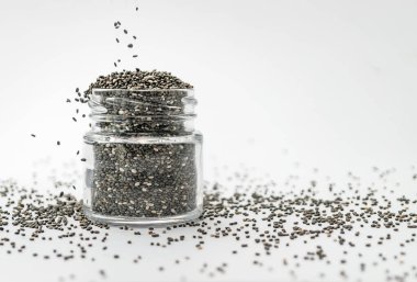 Beyaz arka planda cam kavanoza kuru chia tohumları dökülüyor. İzole edilmiş, kopyalama alanı. Chia süper yemek paleo diyet konsepti.