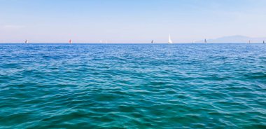 Gün boyunca açık mavi denizde ufukta seyir halindeki yatlar. Yatay kuyruk görüntüsü. Yaz yelken tatili konsepti.