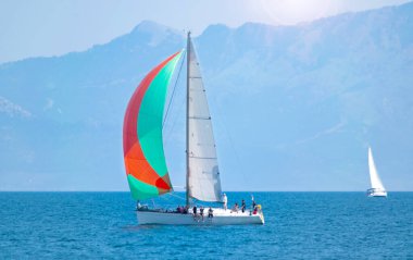 Gündüz açık denizde renkli yelkenli bir yat ve arka planda bir ada. Yachting macera konsepti