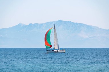 Gündüz sakin denizde renkli yelkenli bir yat ve arka planda açık mavi gökyüzü. Yachting macera konsepti