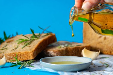 Olive oil pourin into a saucer close up with bread and herbs on bakcground. Mediterranean cuisine concept. Healthy eating habits. Gmo free. clipart