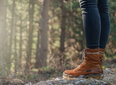 Deri çizmeli kadın bacakları ormanı yakından görüyor, arka planda odaklanmamış ağaçlar var. Yürüyüş turizmi. Dağlardaki orman. Boşluğu kopyala.