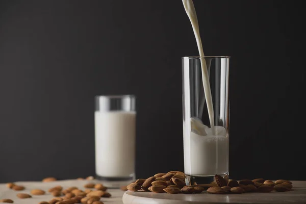 Verter la leche de almendras en un vaso con un vaso de leche sin concentrar sobre el fondo y las nueces de almendras. Leche de almendras sin lactosa concepto sustituto de la leche. Copiar espacio . — Foto de Stock