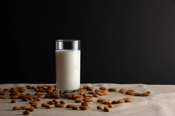 Vaso de leche de almendras sobre mantel de lino con almendras alrededor. Concepto sustitutivo de lactosa. Copiar espacio, fondo negro . — Foto de Stock