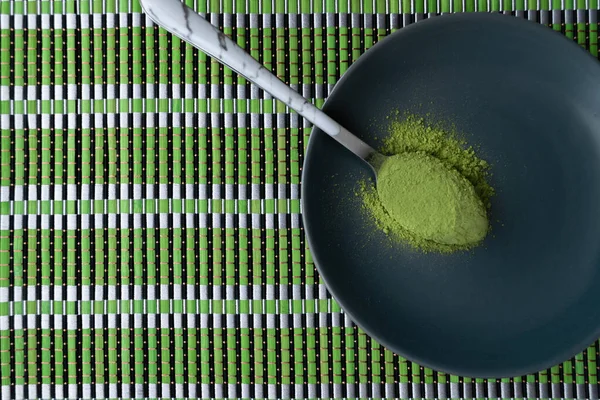 Spoon of matcha green tea powder on black plate on green table. Matcha detox tea making concept. Copy space, flat lay. — Stock Photo, Image