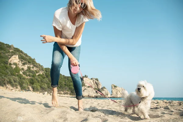 年轻的金发女人和狗在海滩边散步很开心 — 图库照片