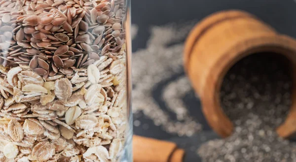 Κλείστε τη βρώμη και τους λιναρόσπορους σε ένα ποτήρι με μη εστιασμένο ξύλινο μπολ με σπόρους chia στο παρασκήνιο. Έννοια της διατροφής Παλαιού. — Φωτογραφία Αρχείου