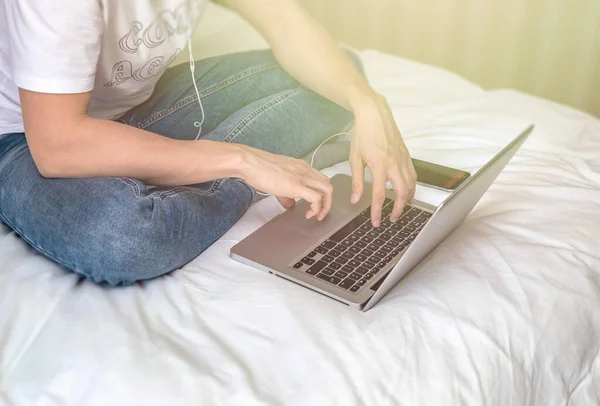 Genç beyaz adam yatakta oturuyor ve laptopta çalışıyor. Evden çalış ve ev konseptinde çalış.. — Stok fotoğraf