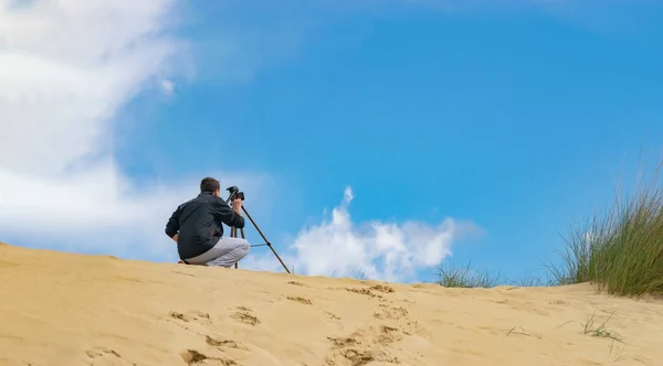 Man setting up mobile phone on tripod for photography and video making in sand hills. Cloudy sky on background. Travel photographer concept.