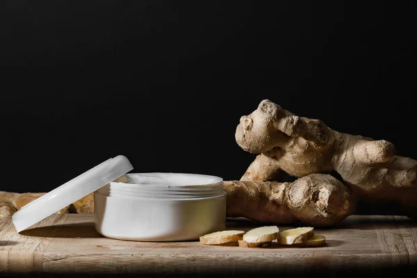 Cosmetics body cream container with ginger oil extract on wooden table. ginger roots and slices. Ginger oil extract cosmetics concept. — Stock Photo, Image