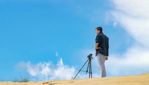 Hombre configurar el teléfono móvil en trípode para la fotografía y la creación de vídeo en colinas de arena. Cielo nublado en el fondo. Concepto de fotógrafo . —  Fotos de Stock