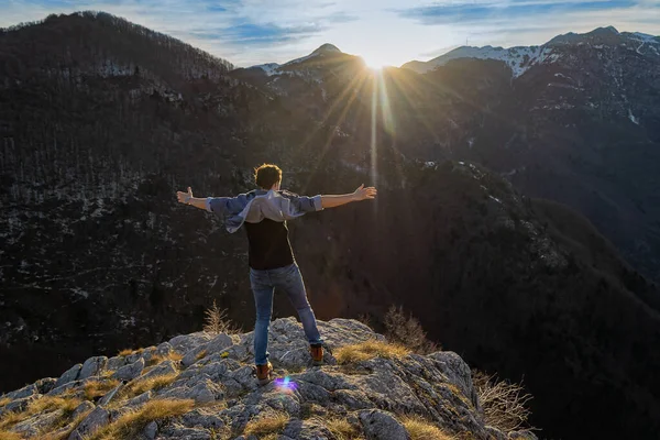 山の中で夕日を眺めながら岩の多い崖の端には 手を広げてやる気とインスピレーションを受けた男が立っています 動機とインスピレーションの概念 勝者のコンセプト — ストック写真