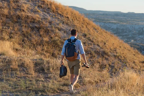 夕日の間に谷を歩くバックパックと三脚を持つ旅行写真家 — ストック写真