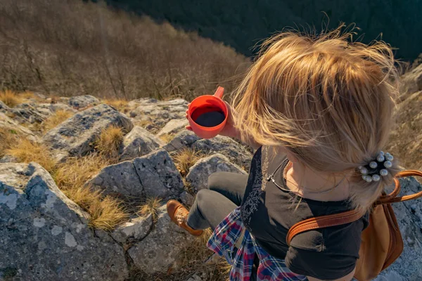 Young woman hiker relaxing with cup of coffee on the edge of cliff enjoying scenic mountains view and sunset. Overhead view. Copy space. Hiking traveler concept.