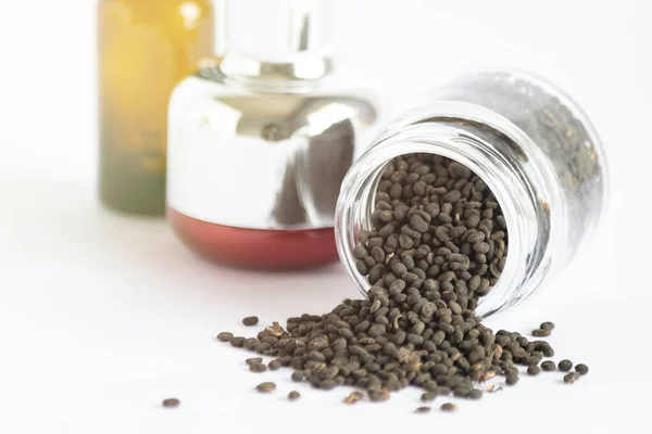 Kuru babchi (Psoralea Corylifolia) tohumları cam kavanozda ve arka planda odaklanmamış kozmetik tüpleri var. Beyaz arka plan, yakın plan. Bakuchiol kavramı.