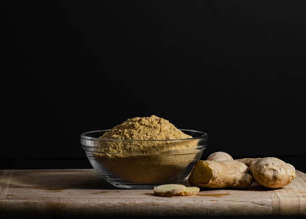 Polvo de jengibre en un recipiente de vidrio sobre tabla de cortar de madera con raíces y rodajas de jengibre. Concepto de alimentación saludable . — Foto de Stock