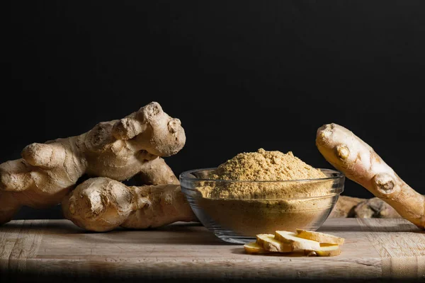 Zencefil kökü ve dilimlerle tahta kesme tahtasındaki cam kasede zencefil tozu. Sağlıklı yeme kavramı.