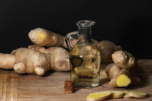 Ginger oil bottle with ginger roots and slices on wooden cutting board. Healthy eating concept. — Stock Photo, Image